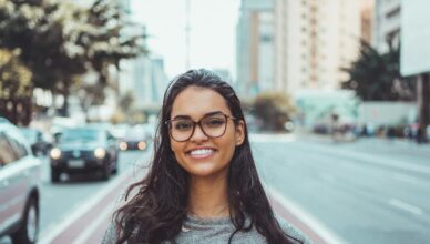 A young woman with glasses smiling on a city street, embracing urban lifestyle.