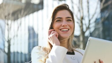 Confident businesswoman using her tablet and phone, smiling outdoors in sunlight.